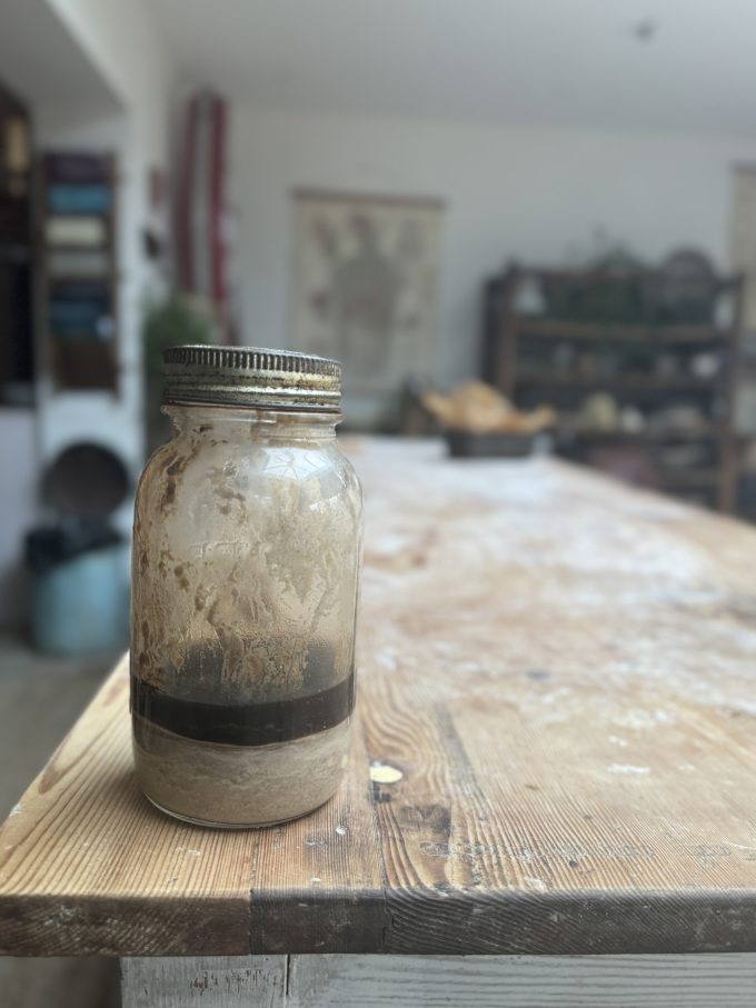 a sourdough starter on the bench at The Sourdough school showing an unrefreshed starter that has formed a hooch on top. the liquid is clear to see. 