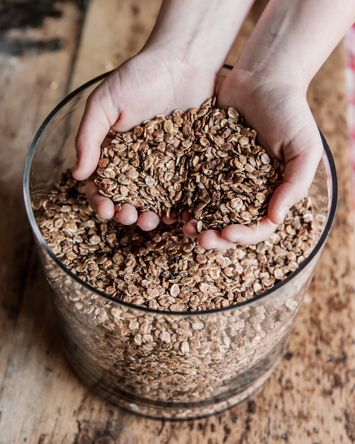 Two hands scooping grain out of a glass jar