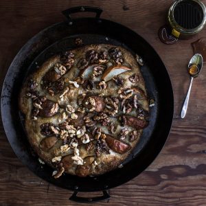 Top view of an autumn pear, honey, and walnut flatbread, featuring a golden-brown crust and garnished with fresh pear slices, walnuts, and a drizzle of honey.