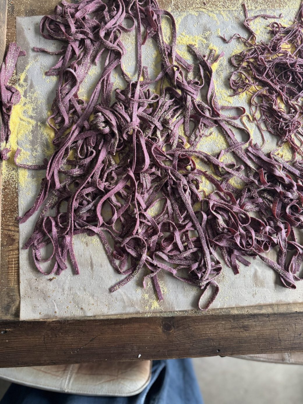 Close-up view of freshly made sourdough pasta strands on a wooden board, showcasing the texture and vibrant colour.