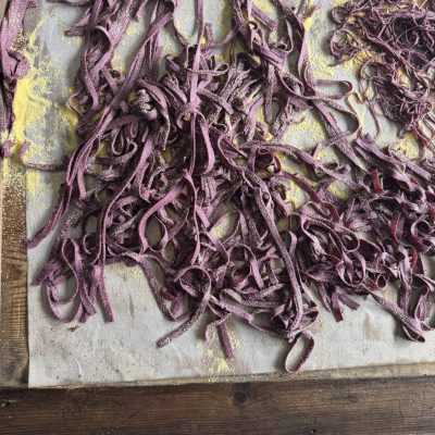 Close-up view of freshly made sourdough pasta strands on a wooden board, showcasing the texture and vibrant colour.