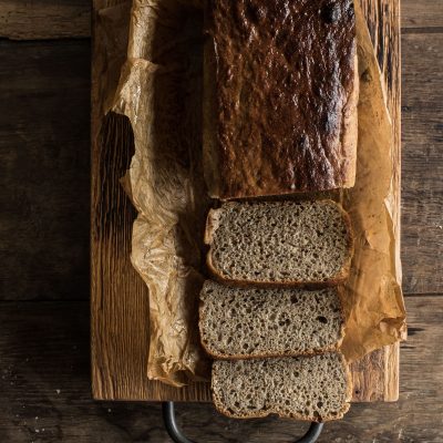 Loaf of sliced homemade bread on parchment paper atop a wooden cutting board.