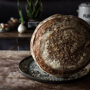 A beer boule topped with barley flakes is standing on its side on top of a black plate placed on a wooden table.