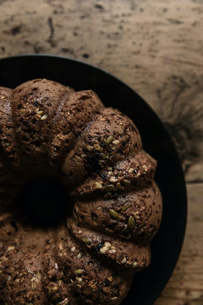 Close up of seeded bundt sweet sourodough on a black plate ontop of a wooden table.